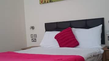 Een hotelkamer met een bed, een rood-witte spreidek, een zwart hoofdeinde, een bloemrijk schilderij aan de muur en een nachtkastje met een lamp.