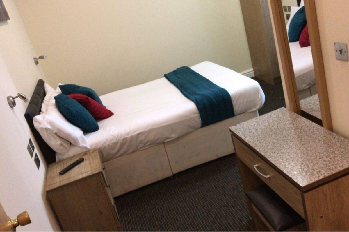 A small, single-bed room with a wooden desk and a mirror.