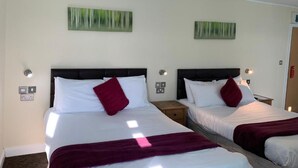 A hotel room with two beds, each with white bedding and red pillows, and a dark headboard. There are two wall-mounted light fixtures on either side of the beds. - Elsinore Hotel (Llandudno)