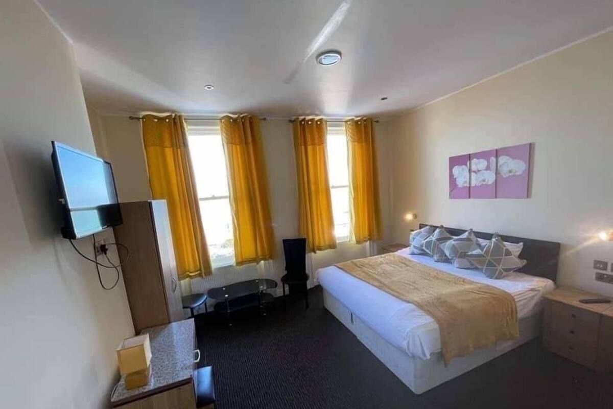 A hotel room with a bed, a desk, a chair, a TV, and a window with curtains.