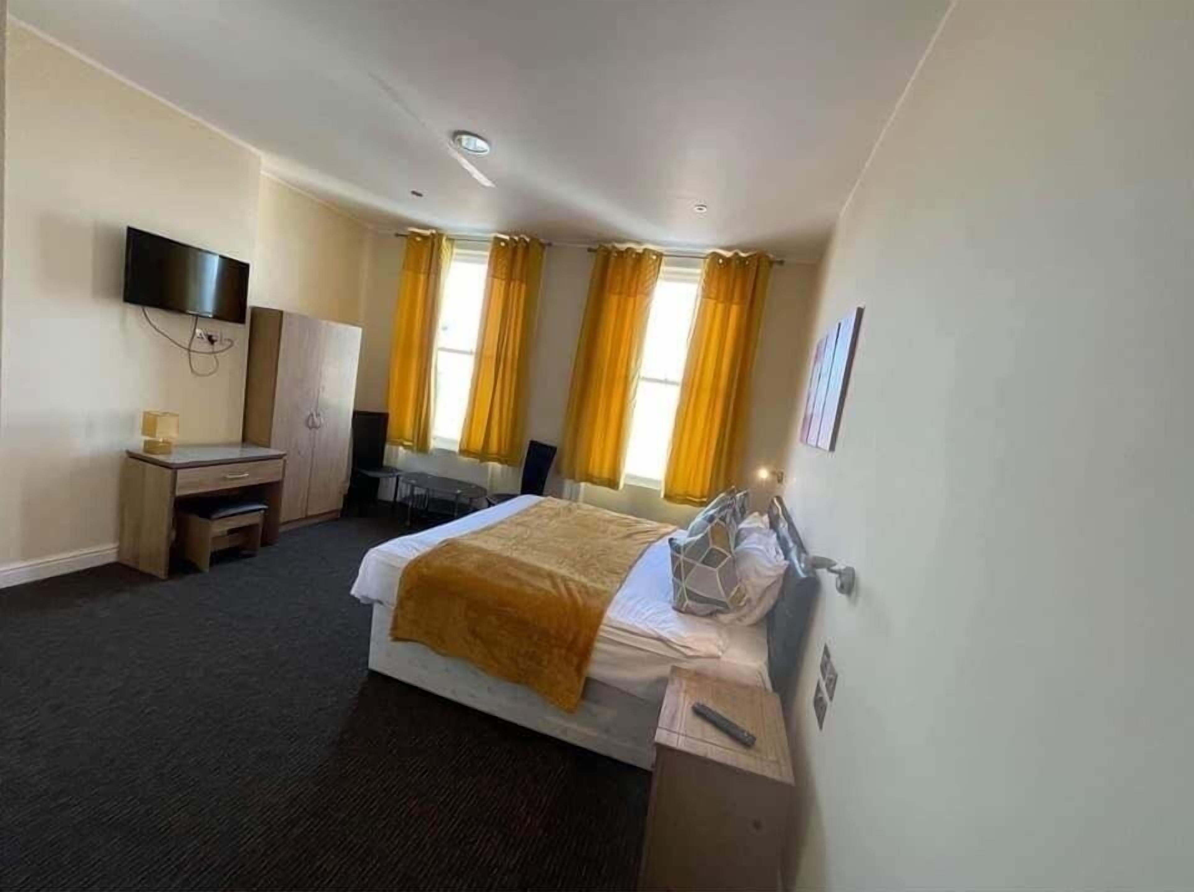 Habitación de hotel con cama, escritorio, silla y televisor montado en la pared.