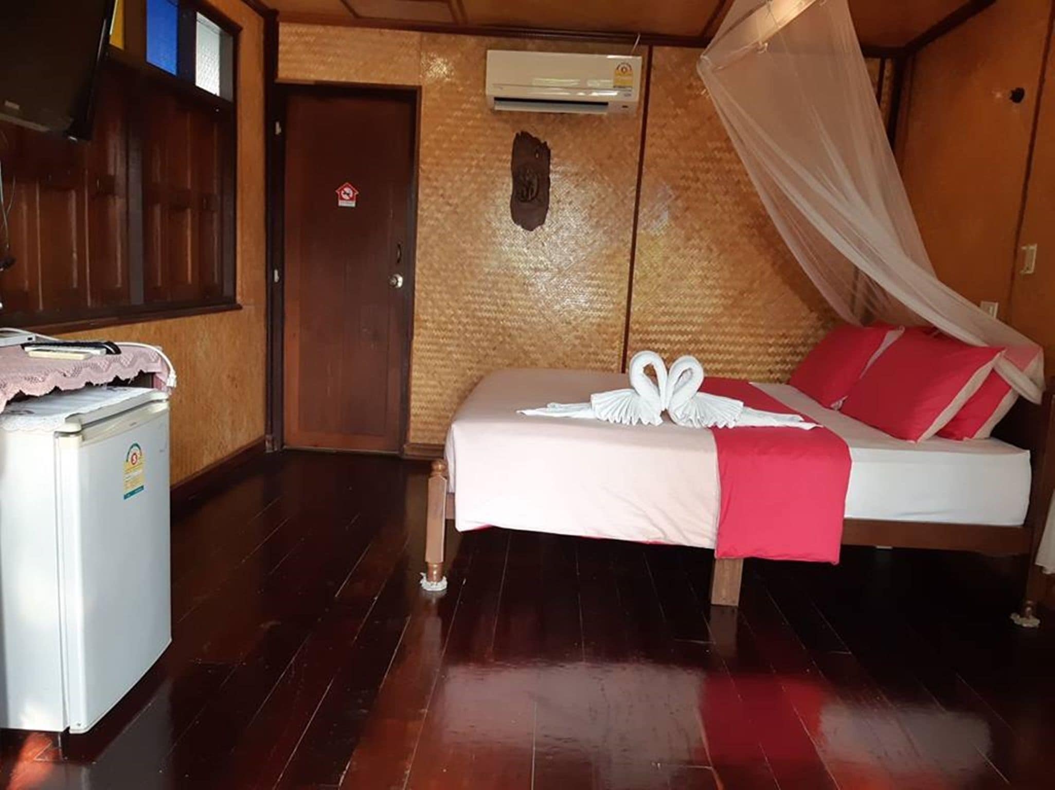 A room with a bed, a small refrigerator, a door, and an air conditioning unit.