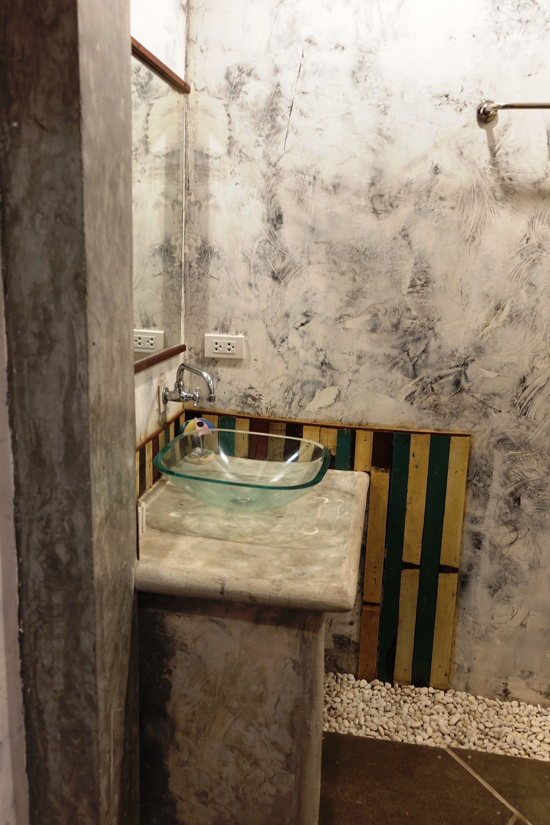 A bathroom with a glass sink, wooden paneling, and a marble wall.