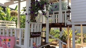 A covered outdoor area with a wooden deck, potted plants, and a hanging flower arrangement. - BaanChompooAmphawa (Amphawa)