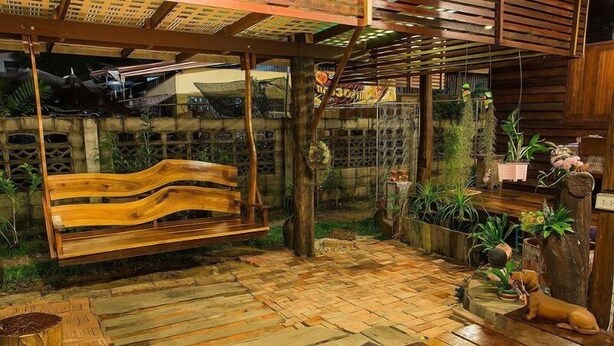 A wooden bench under a wooden pergola, surrounded by potted plants and a small dog statue. - BaanChompooAmphawa (Amphawa)