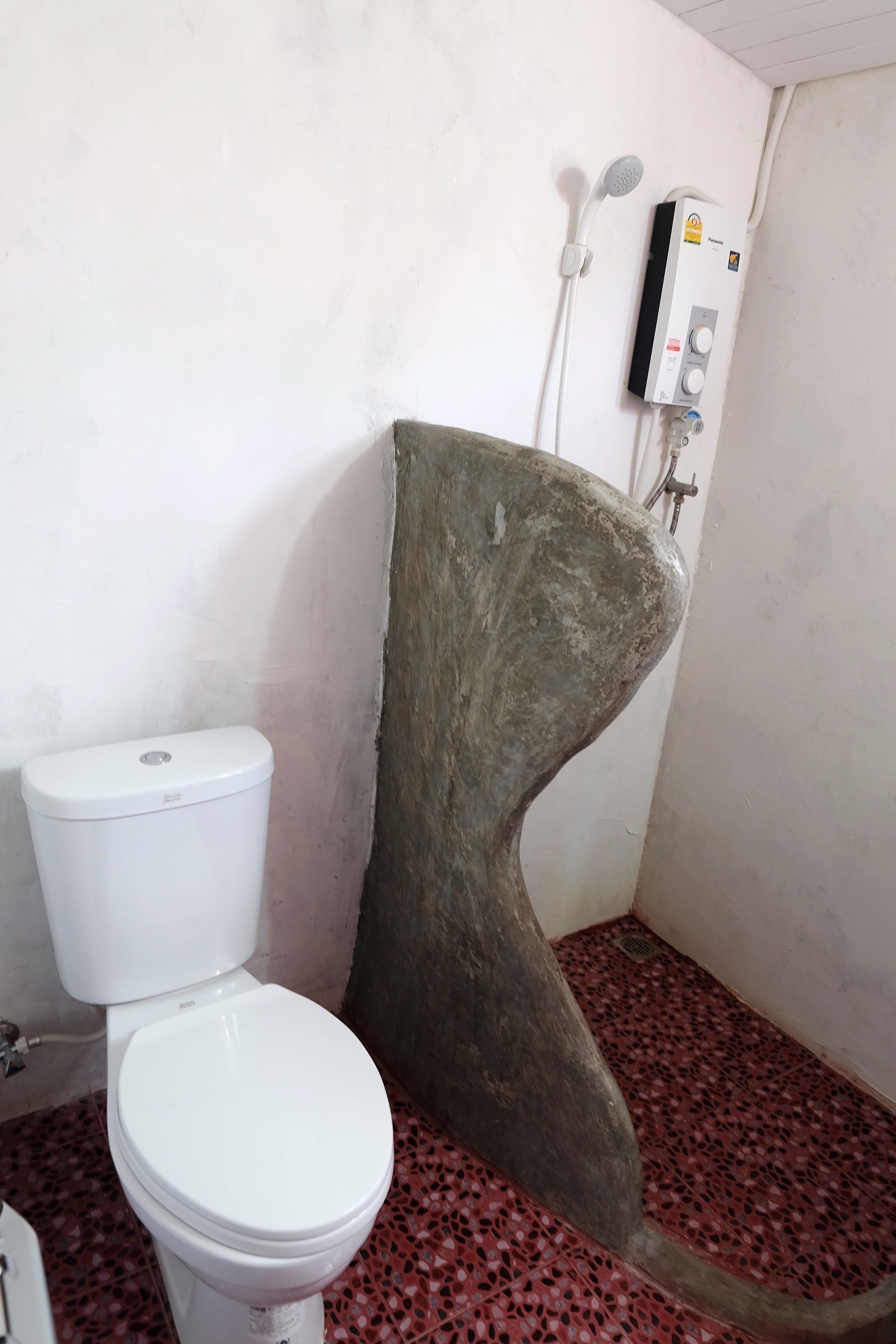 A bathroom with a white toilet, a shower with a control panel, and a red patterned floor.