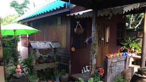 A wooden house with a porch, potted plants, and a small table with items on it. - BaanChompooAmphawa (Amphawa)