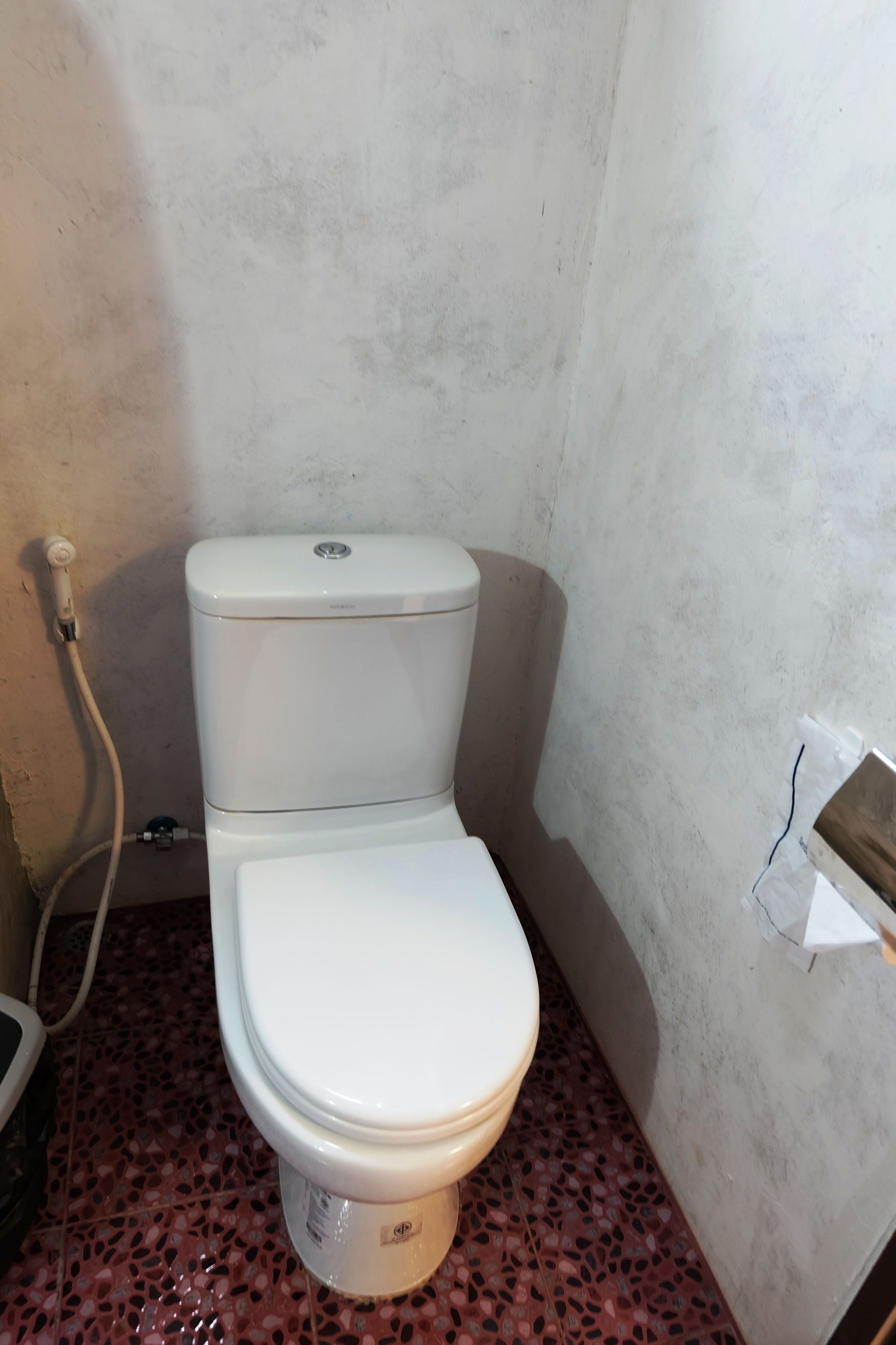 A small bathroom with a white toilet, a red and black speckled floor, and a plain wall.