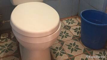 Un inodoro con asiento y tapa blancos, un cubo azul al lado y dos botellas de artículos de aseo en el tanque.