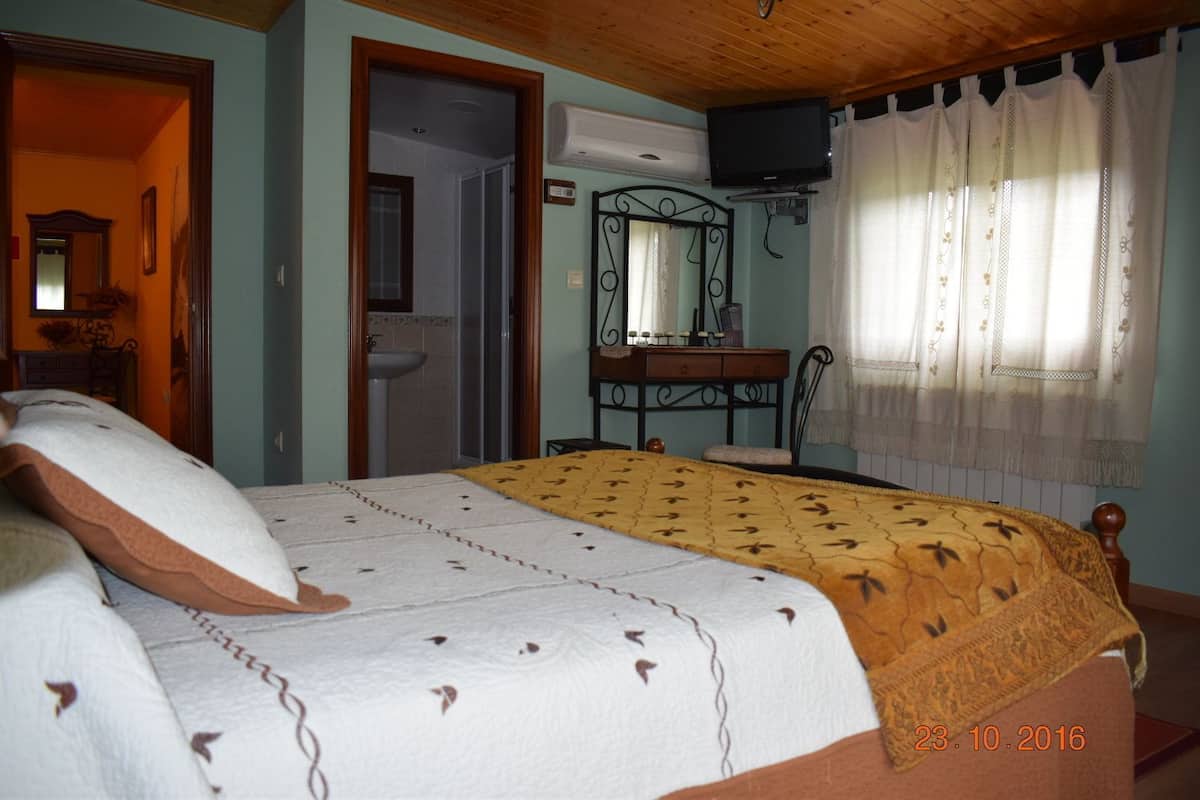 Une chambre à coucher comprenant un lit, un bureau, un miroir, une fenêtre avec des rideaux et une porte donnant sur une salle de bain.