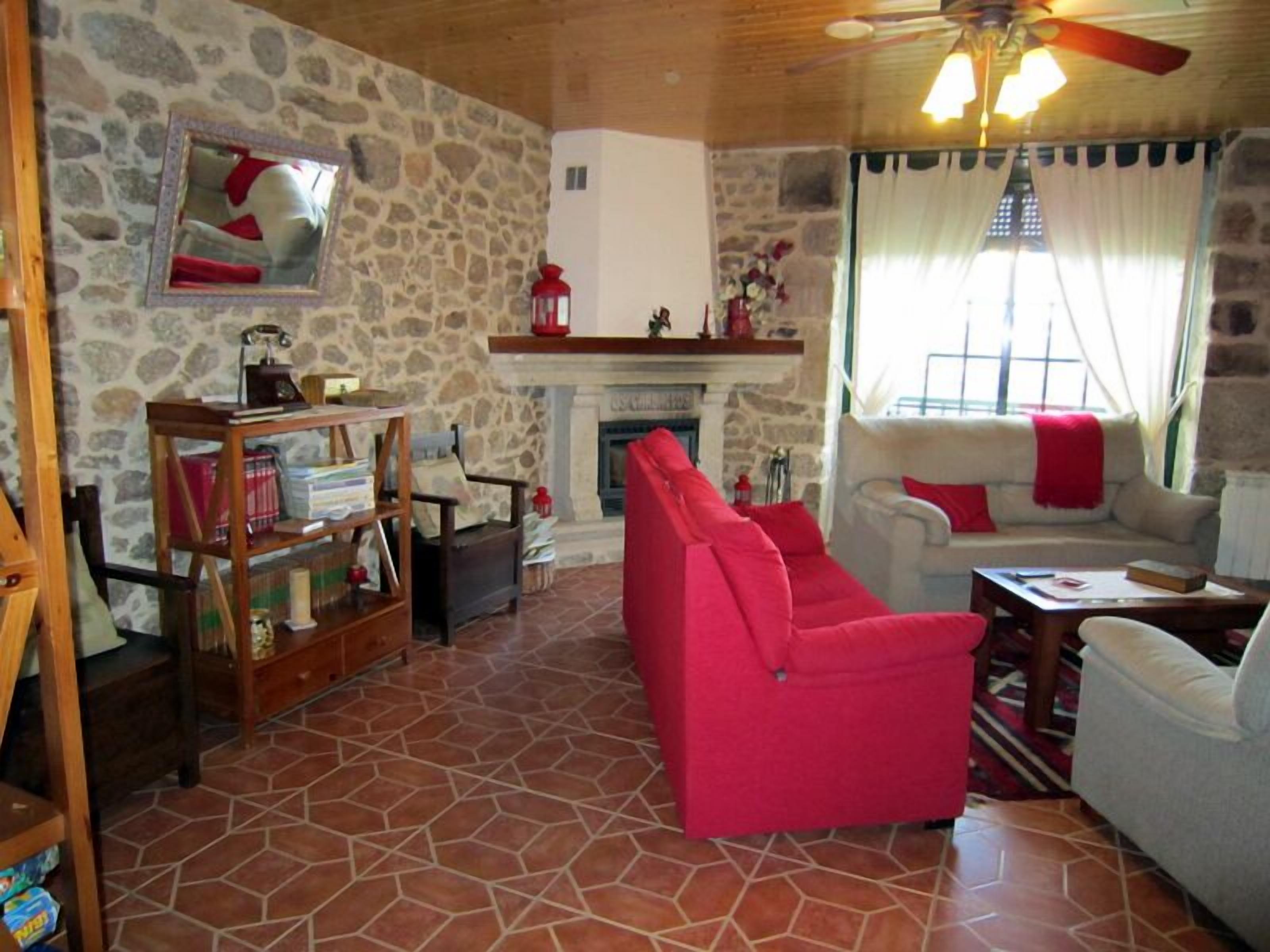 Un salon chaleureux avec un mur en pierre, une cheminée, un canapé rouge et un ventilateur de plafond.
