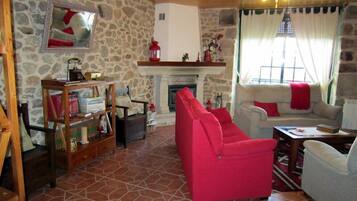 Un salon chaleureux avec un mur en pierre, une cheminée, un canapé rouge et un ventilateur de plafond.