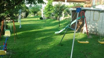 A grassy outdoor area with a swing set and a slide.