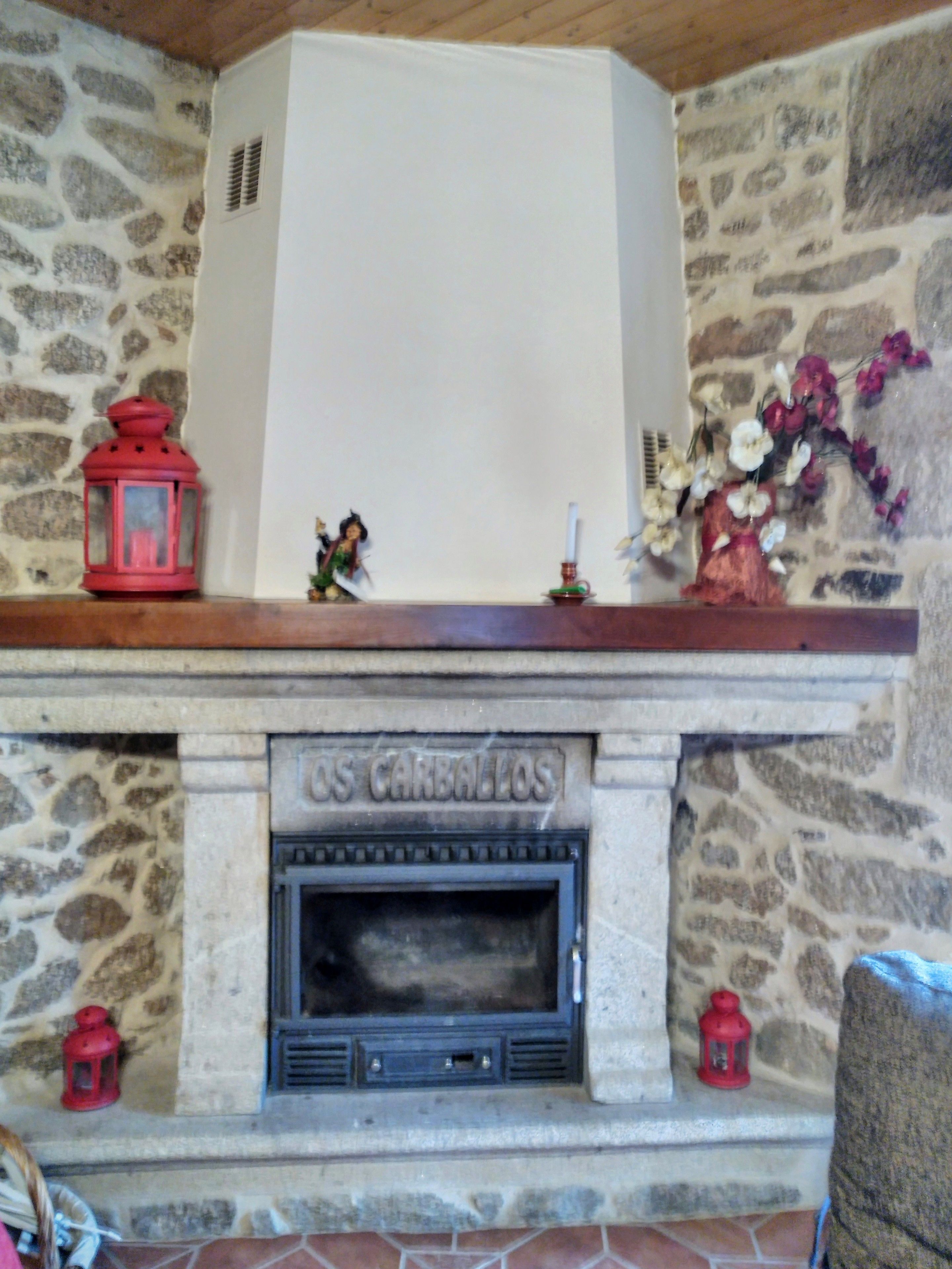 A stone fireplace with a decorative inscription, red lanterns, and a floral arrangement.