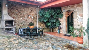 A stone patio with a rustic outdoor seating area, a stone wall, and a large potted plant. - Casa Rural Os Carballos (Barro)
