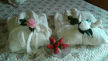Una cama con ropa de cama floral y dos toallas blancas con motivos de flores y fresas.