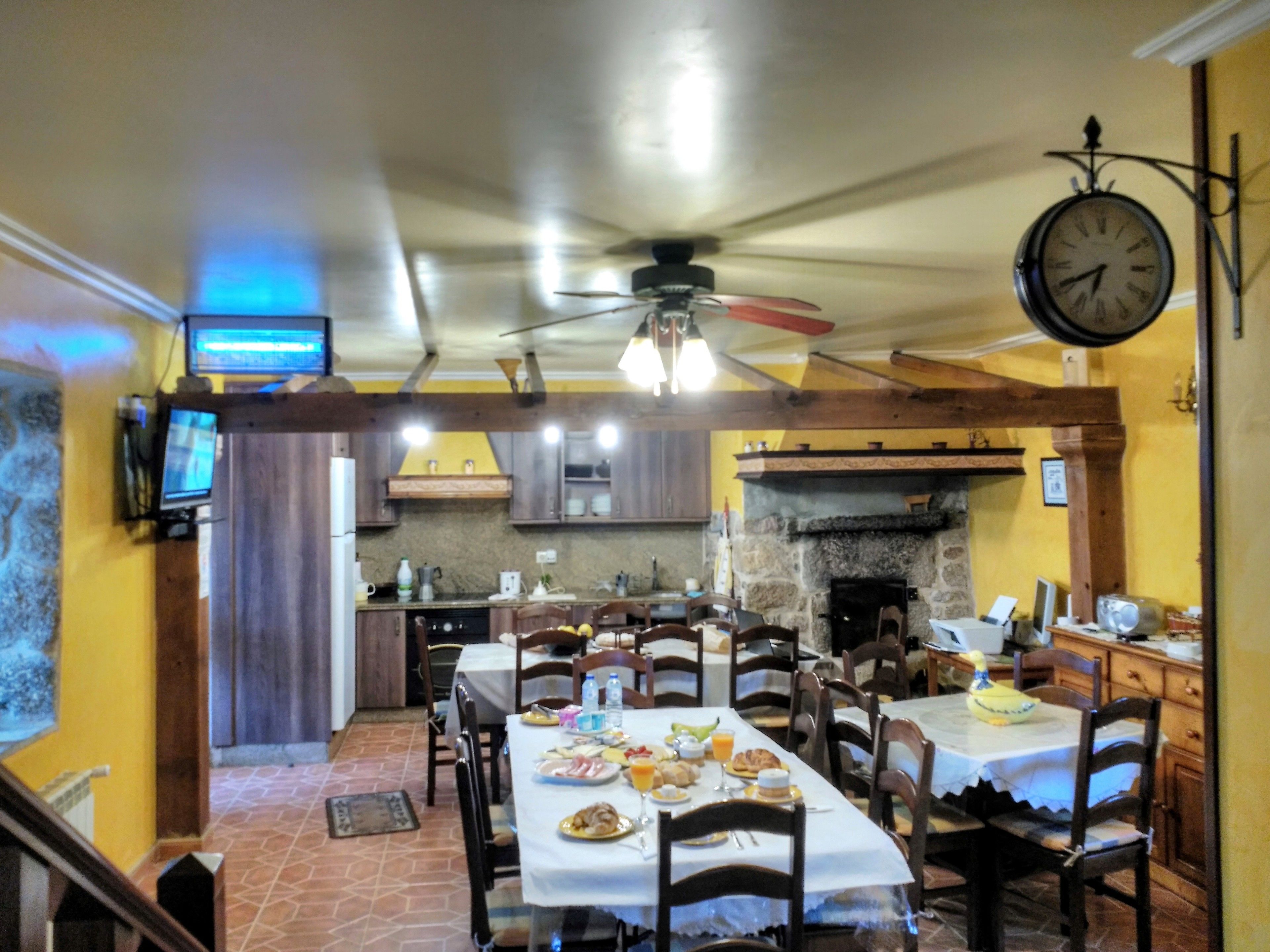 Un comedor con una mesa larga dispuesta para el desayuno, una chimenea de piedra y un reloj en la pared.