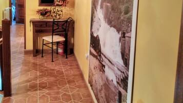 A hallway with a tiled floor, a wooden desk with a chair, a large framed picture on the wall, and a radiator.