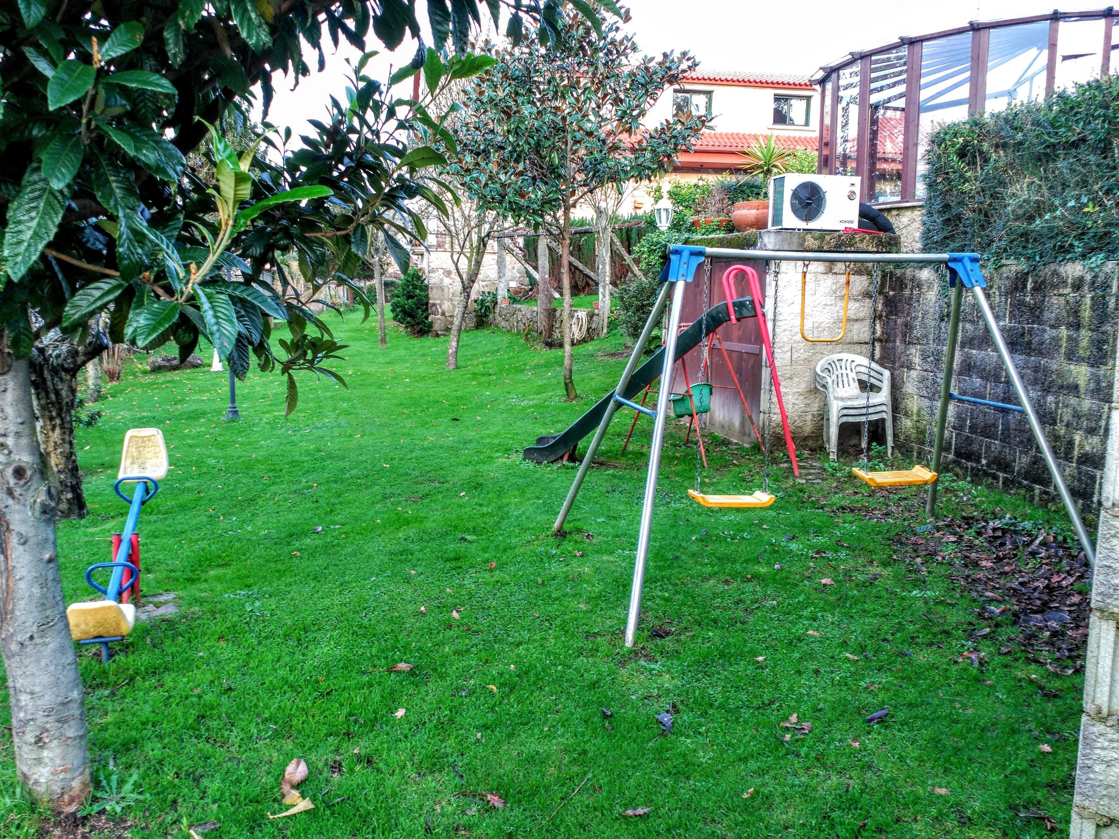 A backyard with a swing set, a small play area, and a tree.