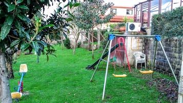A backyard with a swing set, a small play area, and a tree.