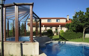 A swimming pool with a glass enclosure, a stone building with a red roof, and a well-maintained garden. - Casa Rural Os Carballos (Barro)