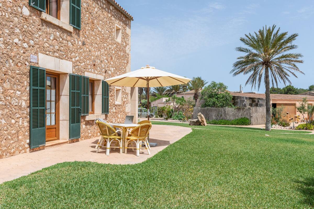 A stone building with a patio area featuring a table and chairs, a large umbrella, and a well-maintained lawn.