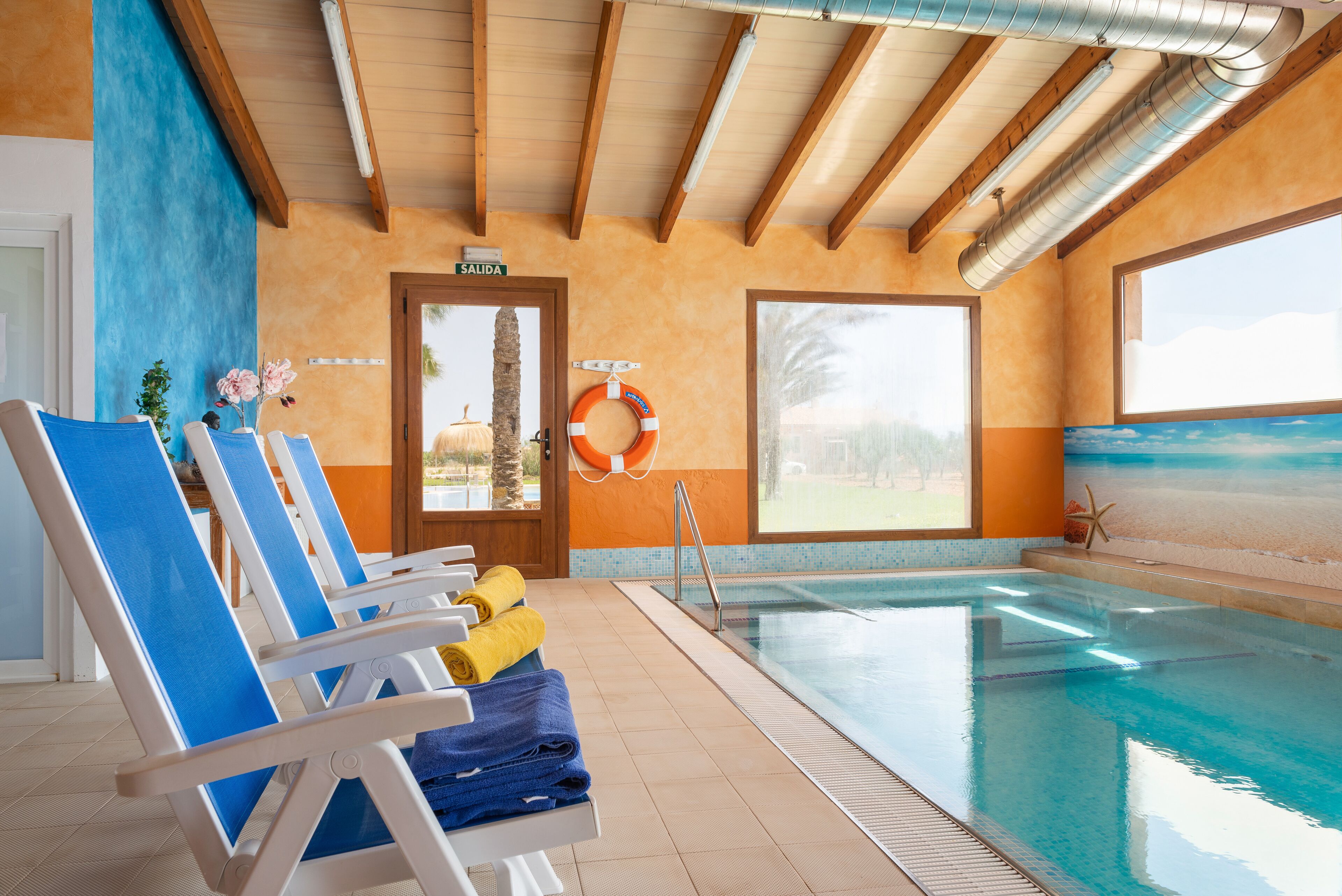 Una piscina interior con sillas de descanso y toallas, un flotador salvavidas y vistas al exterior.