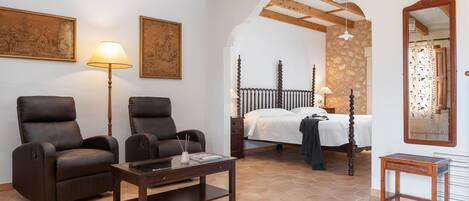 A room with two reclining chairs, a wooden coffee table, a bed with a wooden headboard, and a stone wall.