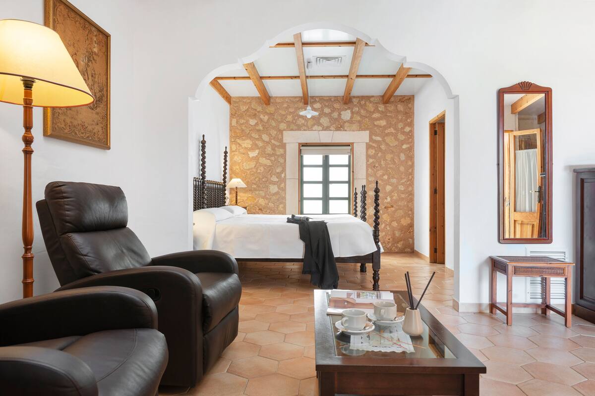 A room with a bed, a leather chair, a table with cups and a tray, a lamp, and a mirror.