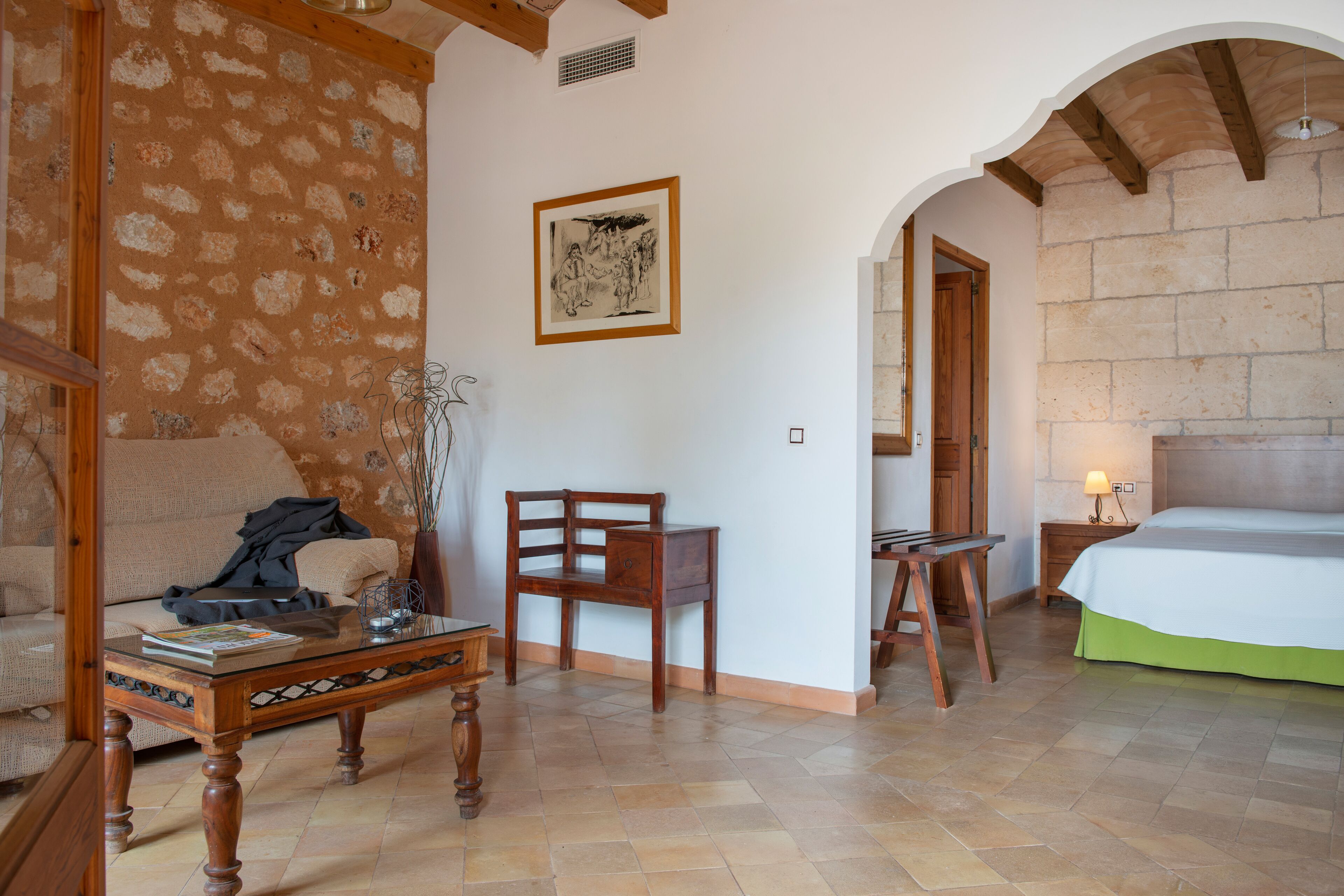 Una stanza con un tavolino in legno, un divano, una poltrona, un letto e un quadro appeso al muro.