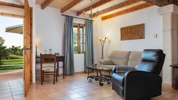 Una sala de estar con un sofá, un sillón, una mesita y una lámpara. Hay una ventana con cortinas y un cuadro en la pared.