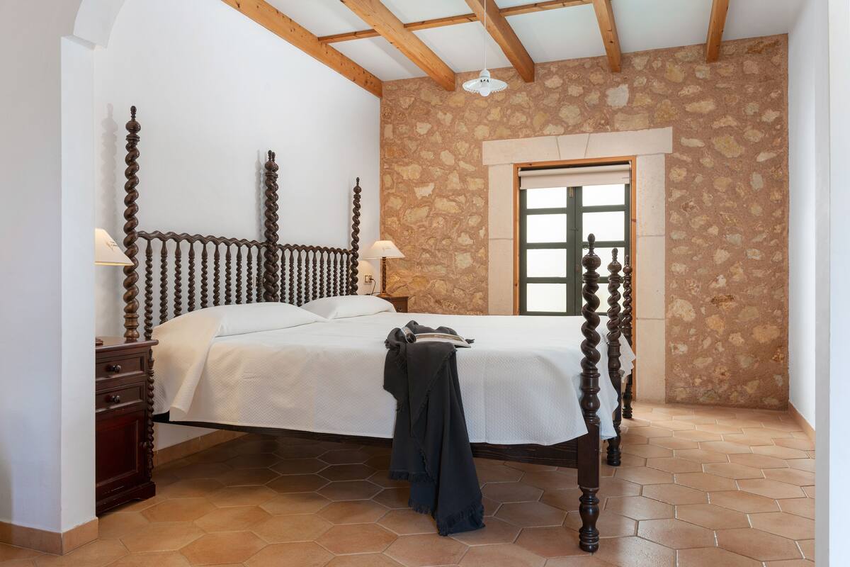 A bedroom with a wooden bed, a stone wall, and a window.