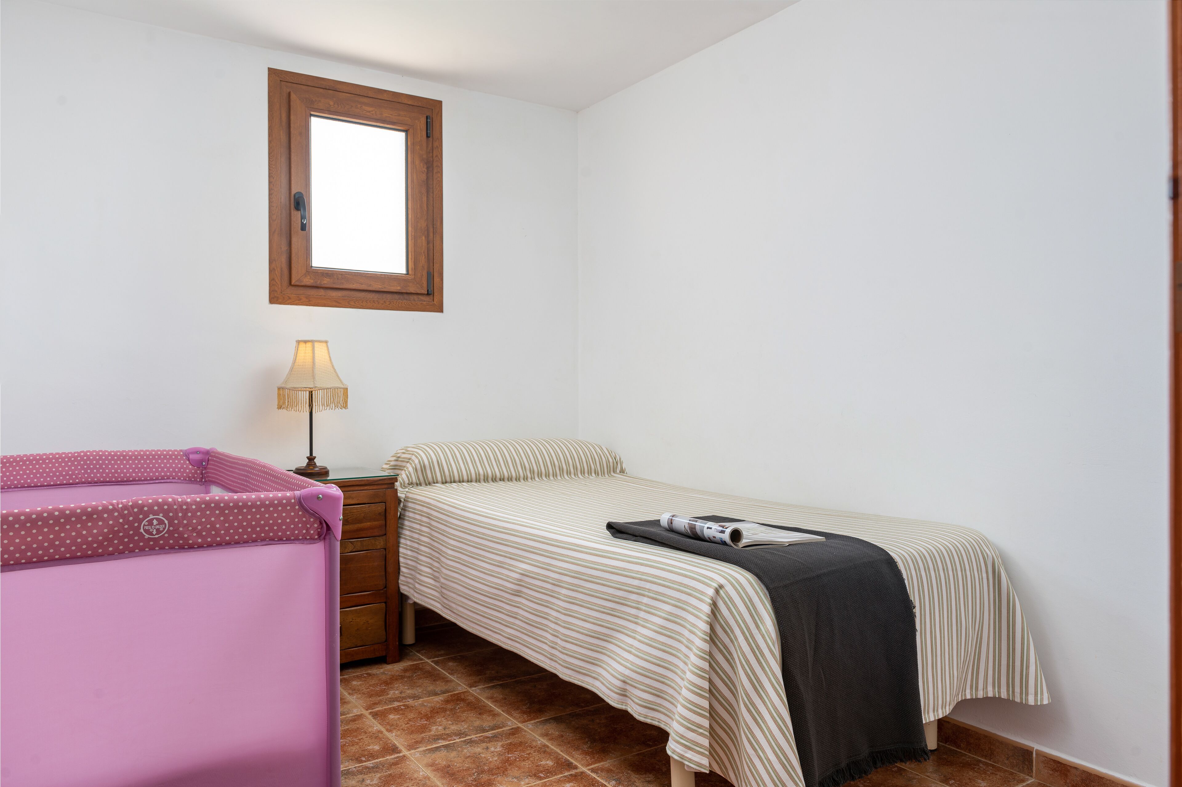 Una habitación pequeña y limpia con una cama individual, una mesita de noche, una lámpara y un mueble de almacenamiento rosa.