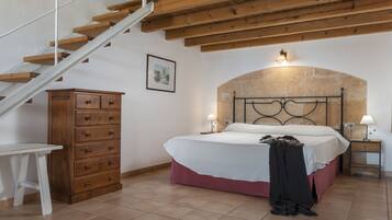 Un dormitorio con una escalera de madera, una cama con cabecera, una mesita de noche, un aparador y un cuadro en la pared.
