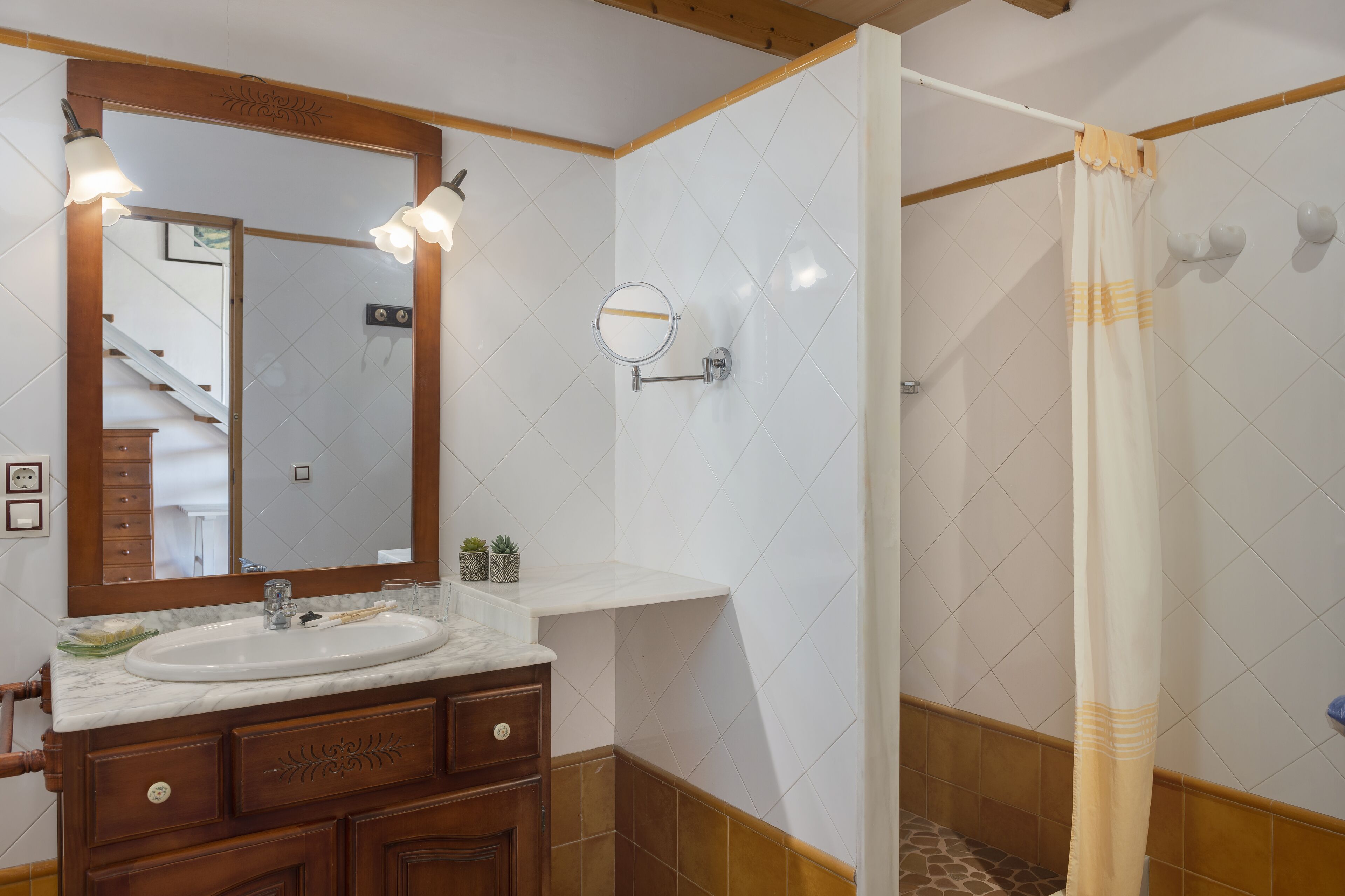 Un baño con tocador de madera, lavamanos, espejo y ducha con cortina.