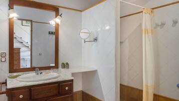 Un baño con tocador de madera, lavamanos, espejo y ducha con cortina.