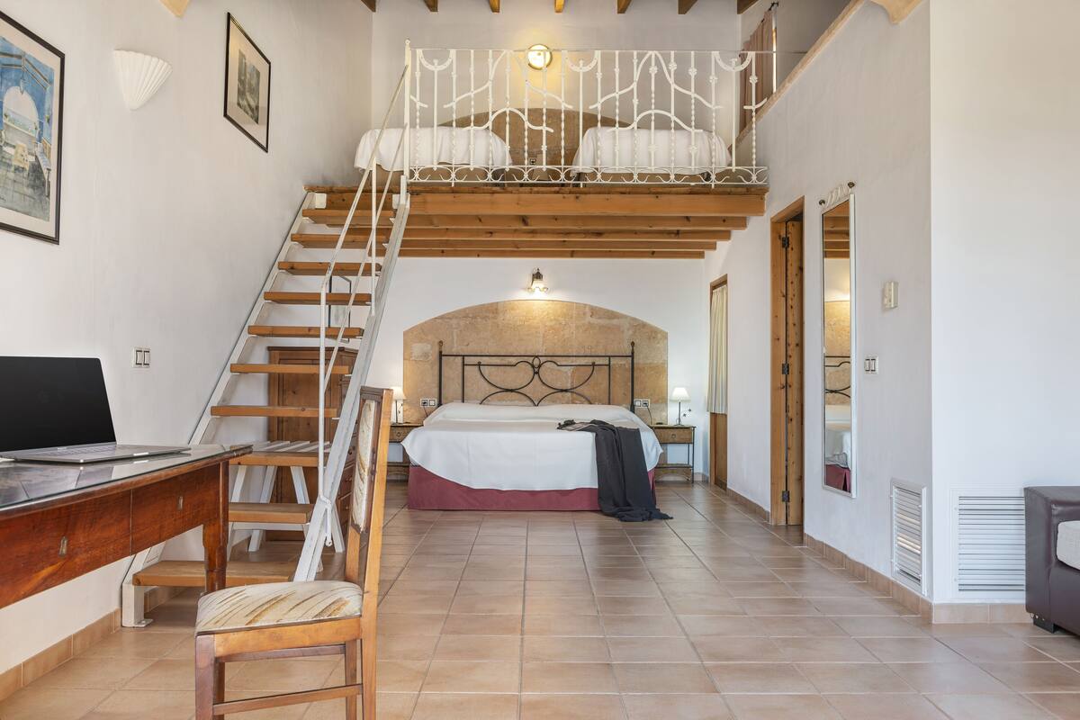 A bedroom with a large bed, a desk, a chair, a staircase, and a loft area.