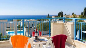 A balcony with a view of the sea, a pool, and a table with chairs. - Philippos Villas (Chlorakas)