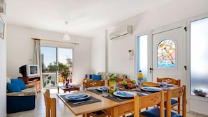 A dining area with a table set for four, a sofa, a TV, and a door with a stained glass window. - Philippos Villas (Chlorakas)