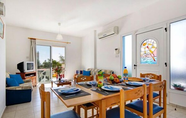 A dining area with a table set for four, a sofa, a TV, and a door with a stained glass window.