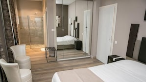 A modern hotel room with a bed, a seating area with chairs, a small table, and a shower area. - Villa Fani (Thiers)