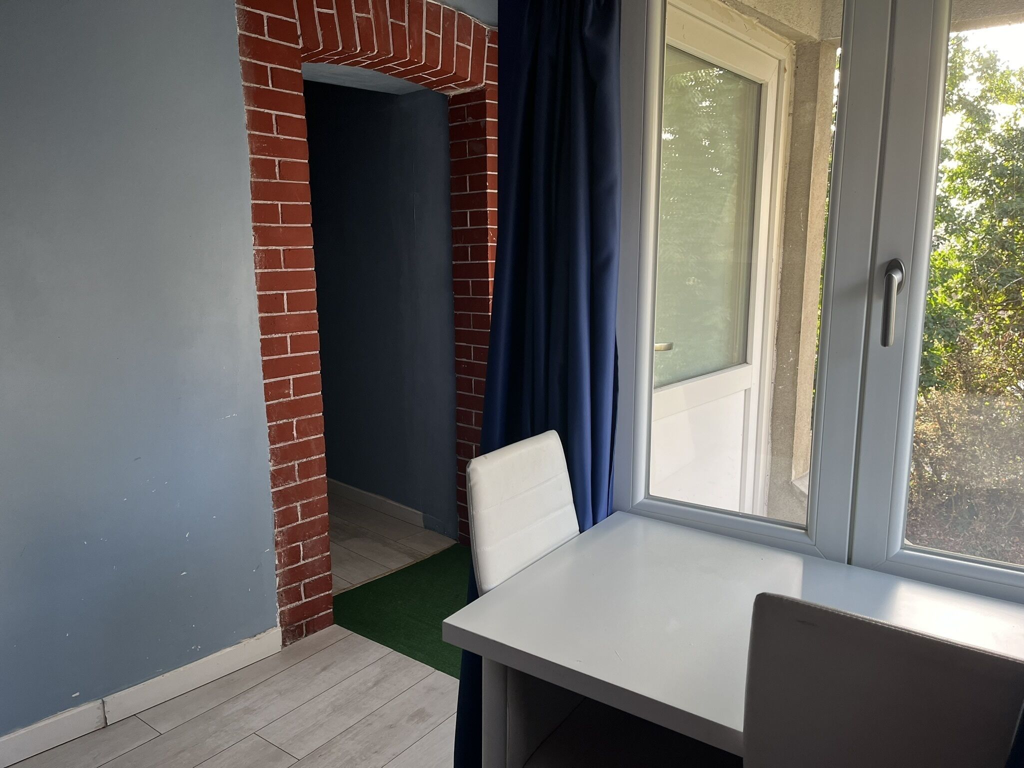 Una stanza con un tavolo bianco, una tenda blu e un muro in mattoni.