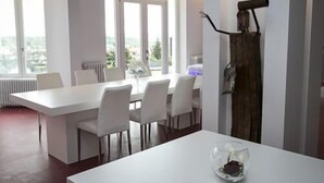 A modern dining area with a white table and chairs, large windows, and a view of greenery. - Villa Fani (Thiers)
