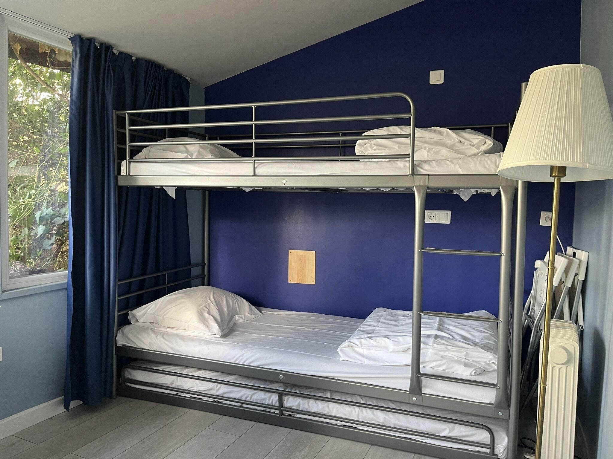 Habitación con literas, ventana, cortinas, lámpara y enchufe en la pared.