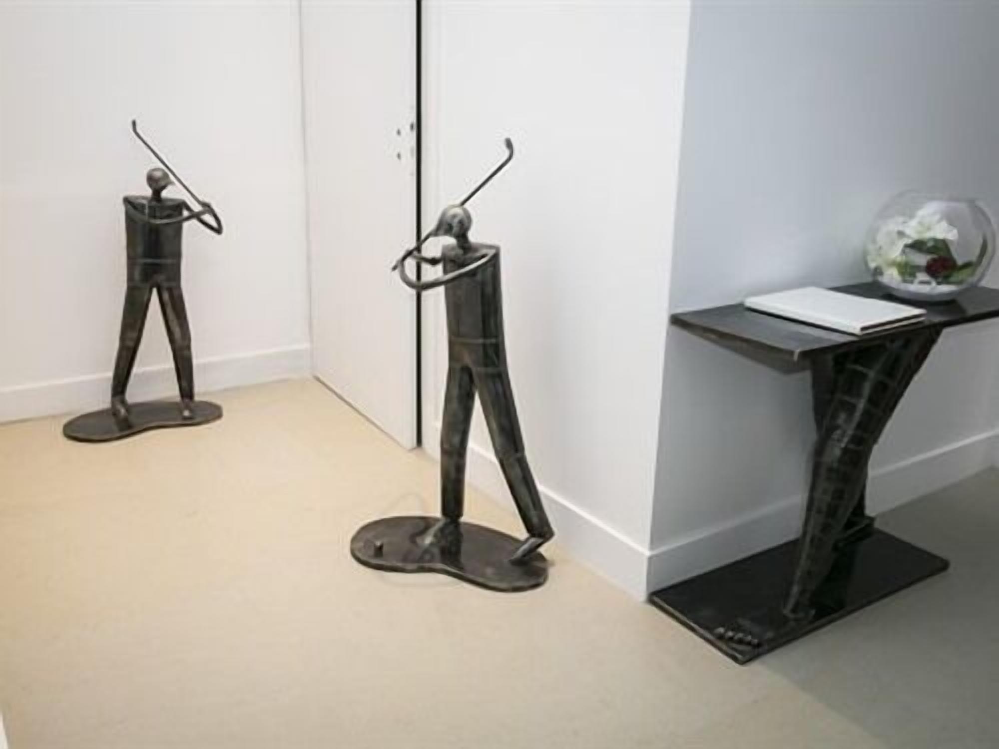Two abstract sculptures in a hallway with a small table and a glass sphere on it.