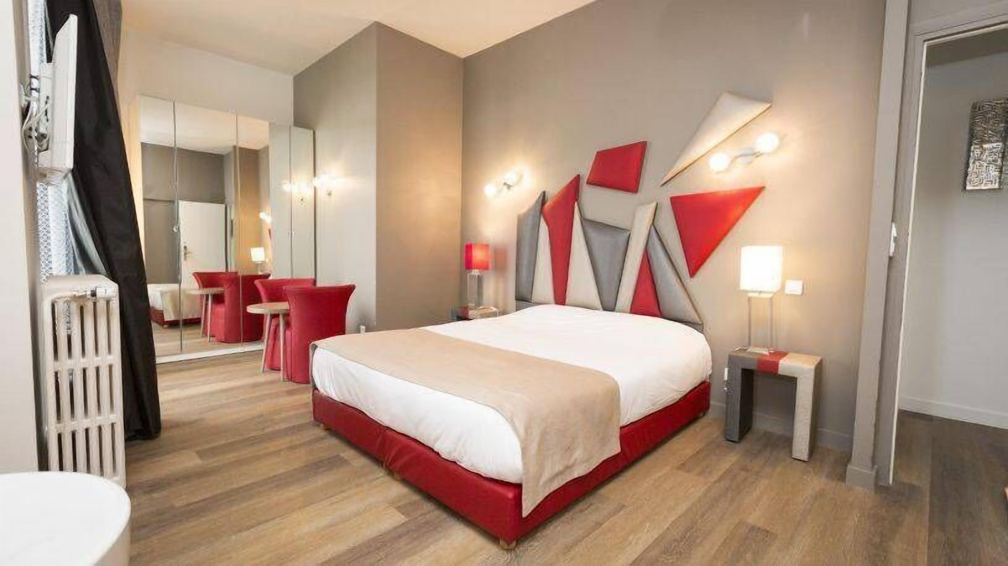 A modern hotel room with a large bed, red accents, and a mirror.