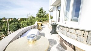 A balcony with a round table and two side tables, a stone wall, and a view of greenery and houses in the background. - Villa Fani (Thiers)