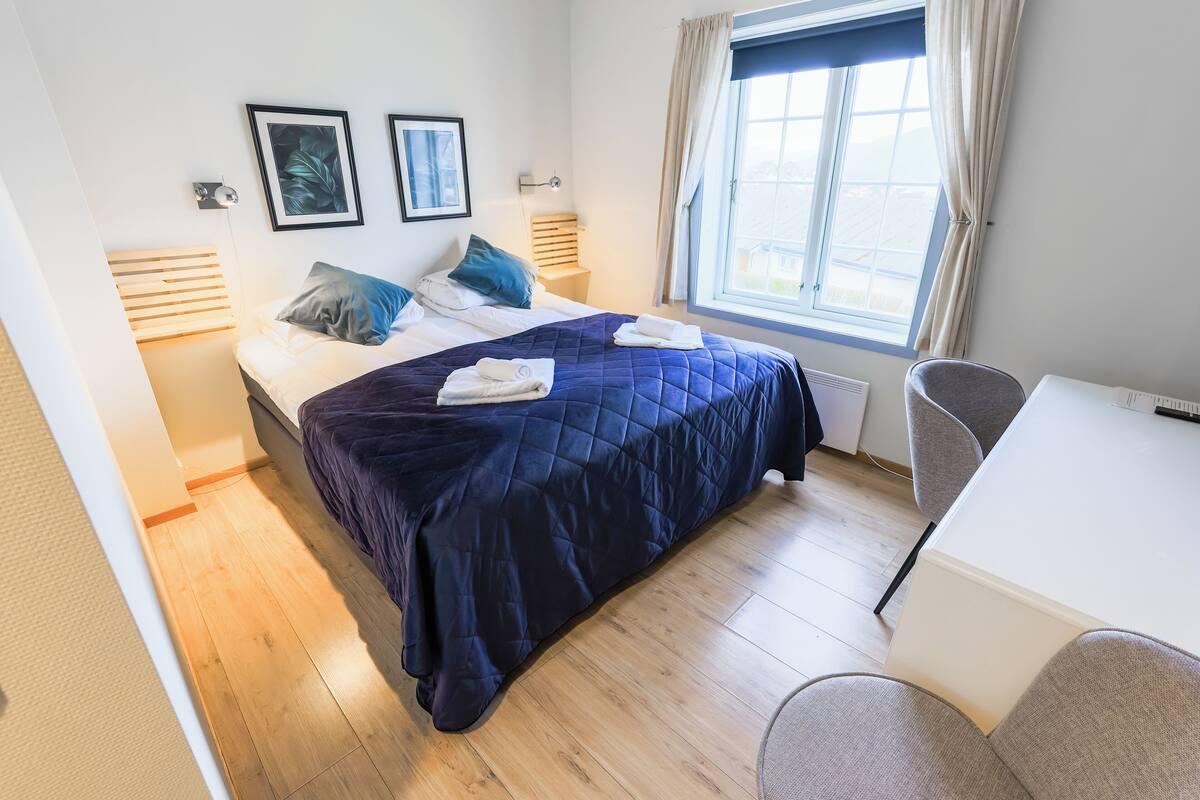 Ein Hotelzimmer mit Bett, Nachttischlampen, einem Schreibtisch und einem Fenster mit Vorhängen.