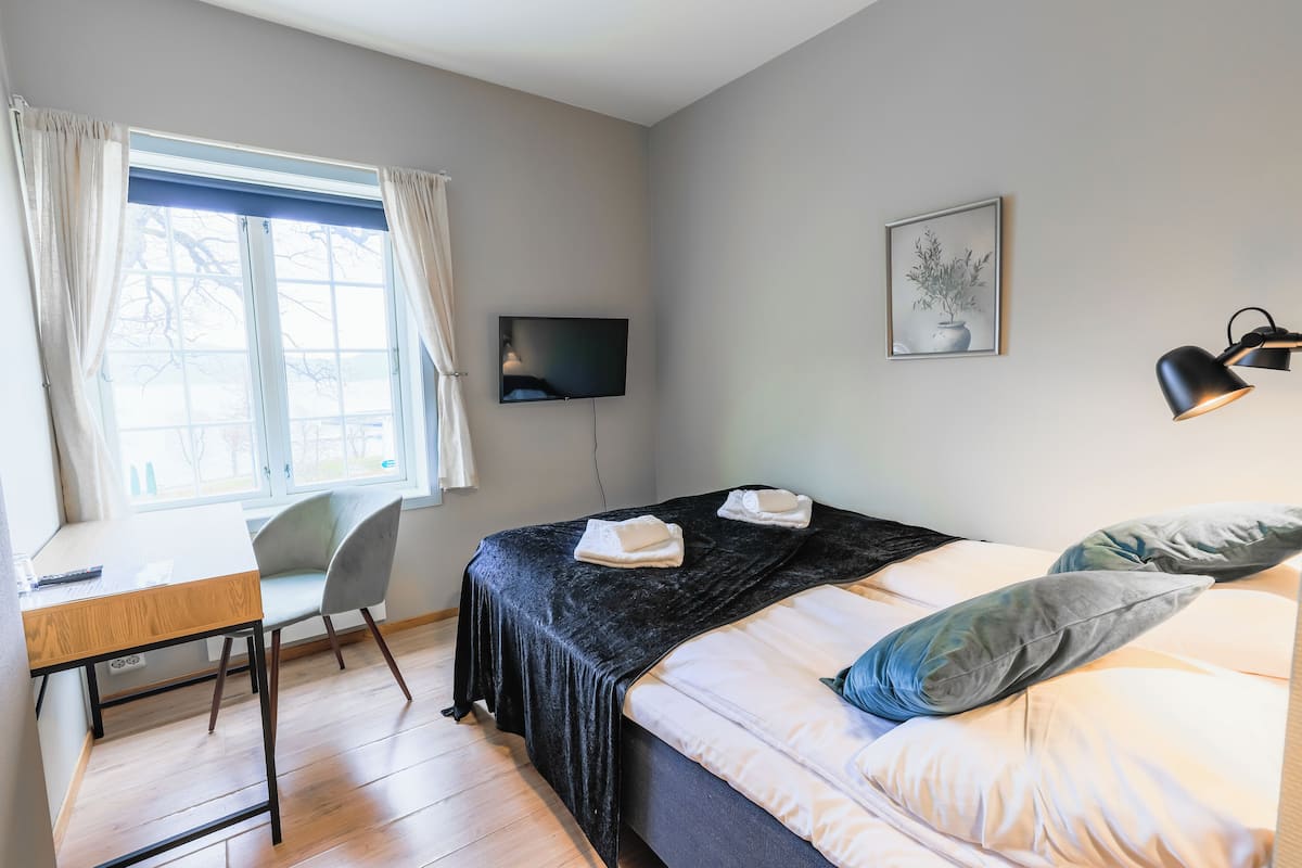 Ein Schlafzimmer mit Bett, Schreibtisch, Stuhl, Fernseher und einem Fenster mit Vorhängen.
