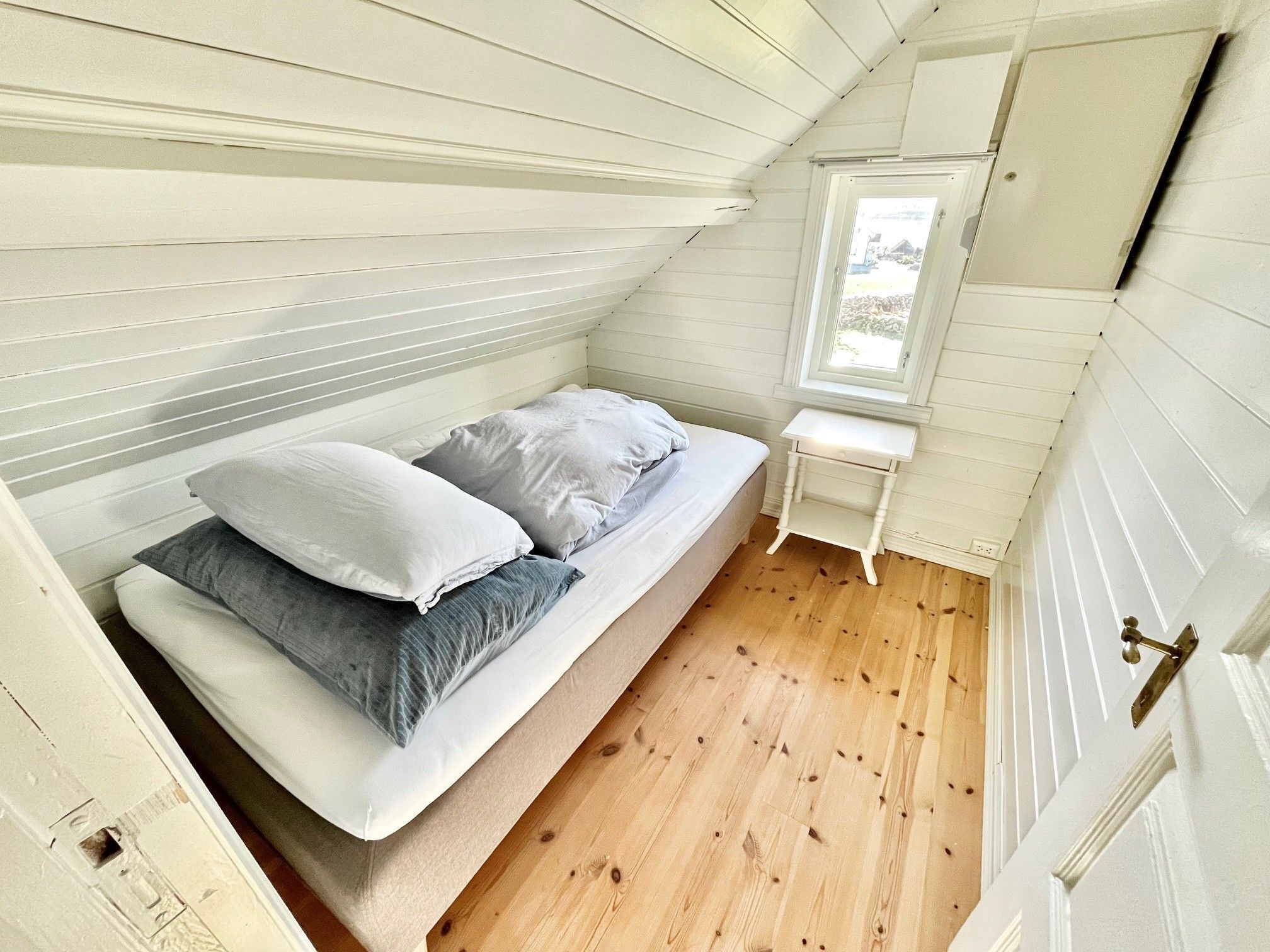 Ein kleines, gemütliches Schlafzimmer mit einem Einzelbett, einem Fenster und einer weißen Tür.
